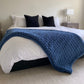 Medium chunky knit blanket in Cold Sea draped over a king bed.