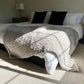 Small chunky knit blanket in Grey draped over the edge of a king bed as a throw blanket.