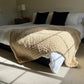 Small chunky knit blanket in Taupe draped over the edge of a king bed as a throw blanket.