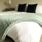 Medium chunky knit blanket in Misty Green draped over a king bed.