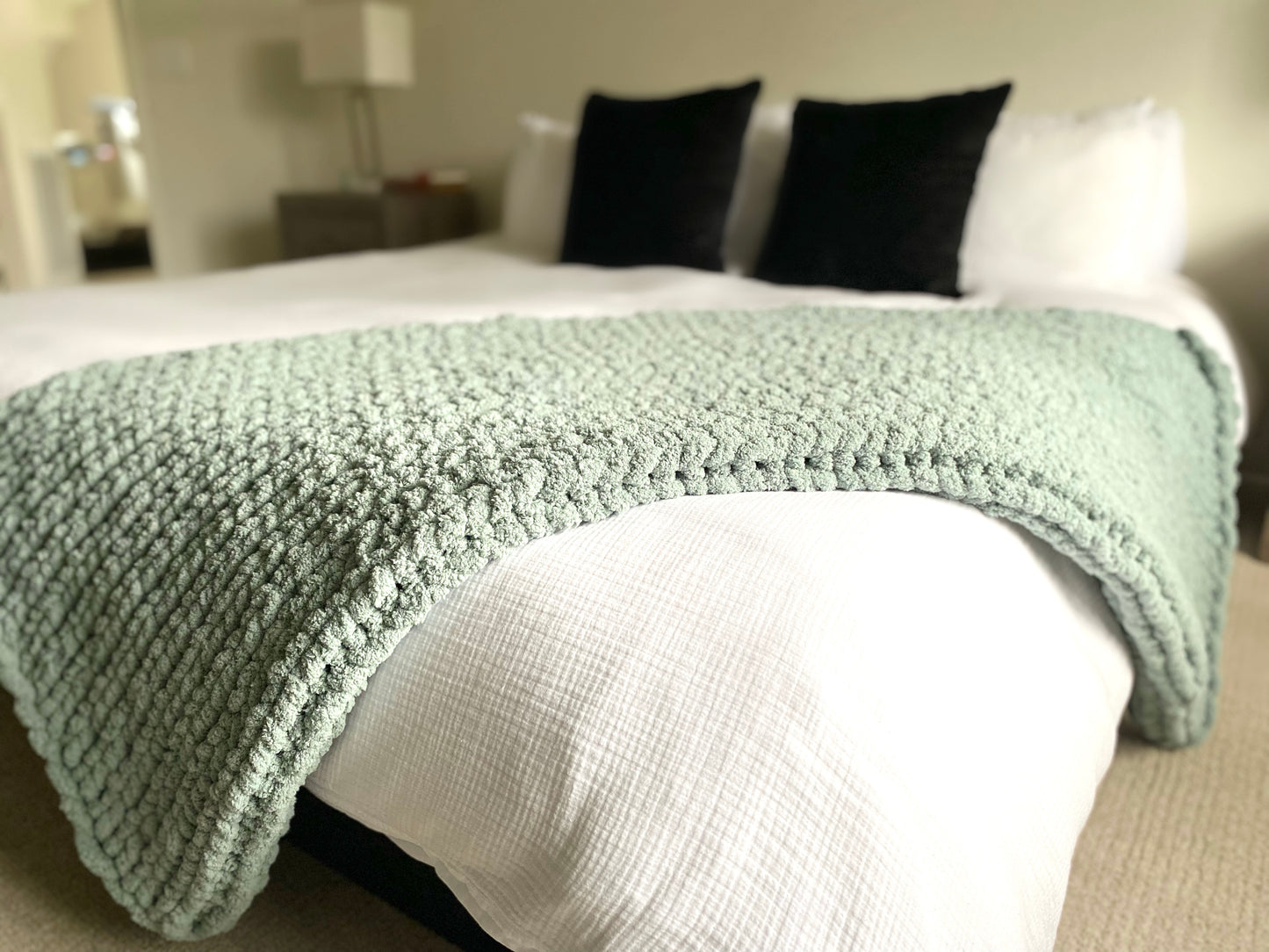 Medium chunky knit blanket in Misty Green draped over a king bed.